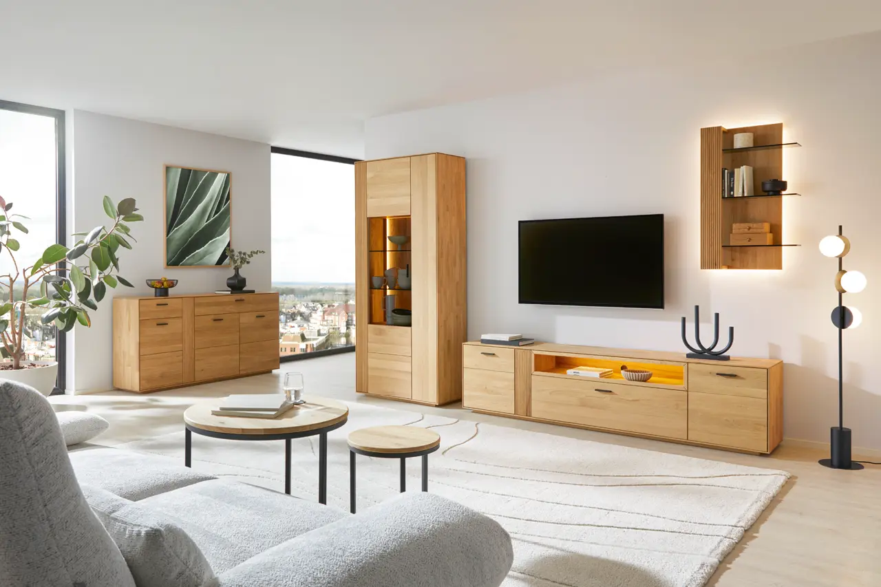 Wohnzimmer mit Holz Wohnwand, Sideboard und Vitrine, grauem Sofa, zwei runden Couchtischen, grosser Fensterfront mit Stadtblick und grosser Pflanze.